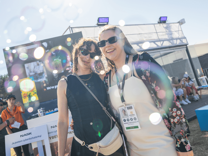 Uczestniczki festiwalu na tle stoiska NASK i Ministerstwa Cyfryzacji. 