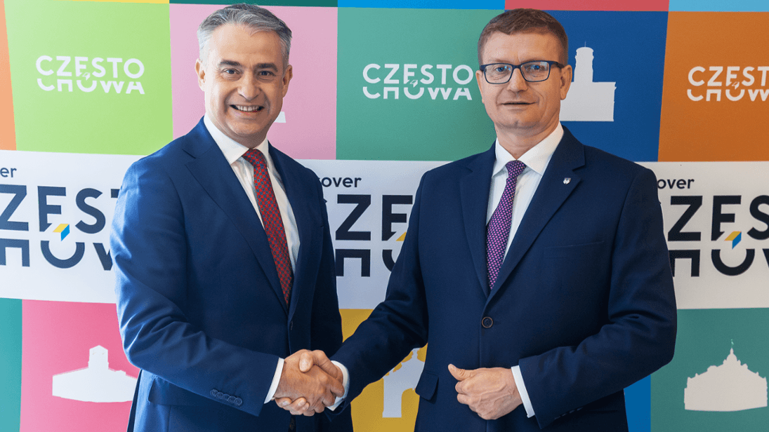 Na zdjęciu Krzysztof Gawkowski i Krzysztof Matyjaszczyk stoją obok siebie, uśmiechając się i podając sobie dłonie. Obaj ubrani są w eleganckie, ciemne garnitury z krawatami. W tle widoczna jest kolorowa ściana z logotypami i napisem „Częstochowa”.