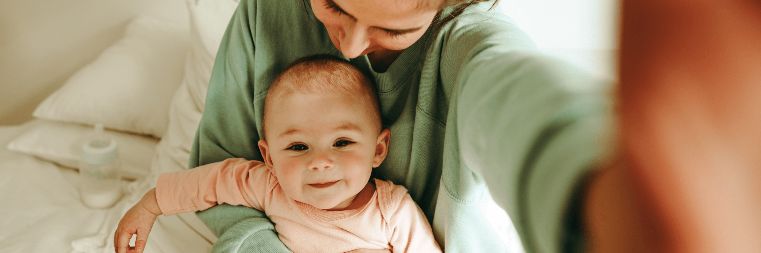 Kobieta obejmuje jedną ręką siedzące na kolanach uśmiechnięte, około roczne dziecko