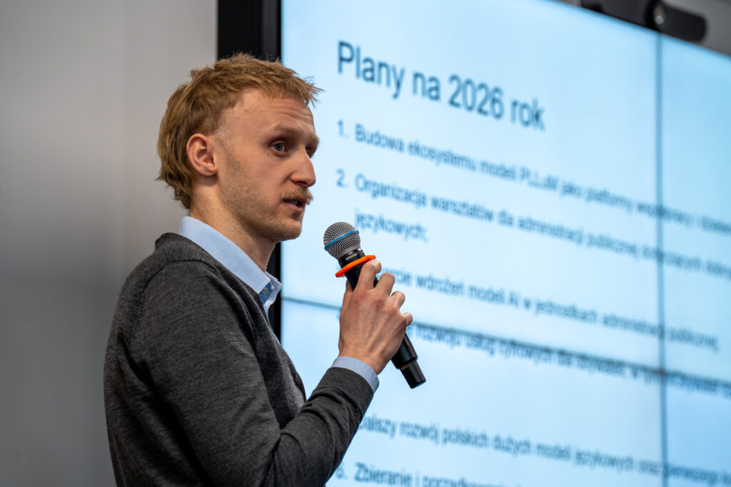 Prelegent z mikrofonem w ręku na tle slajdu.